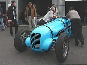 Photo d'une monoplace bleue que deux hommes poussent vers l'arrière en direction d'un garage.