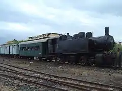 Locomotive à vapeur noire dans la gare de Massaoua tirant deux wagon vert et blanc.