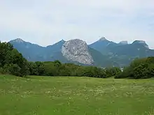 Montagne inclinée s'élevant par-delà une prairie, au-dessus d'une vallée, avec d'autres montagnes en arrière-plan.