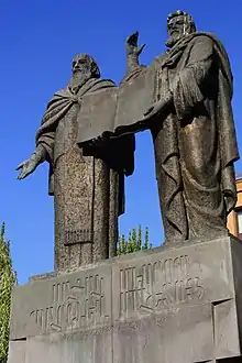Statues de deux hommes côte à côte, présentant un livre.