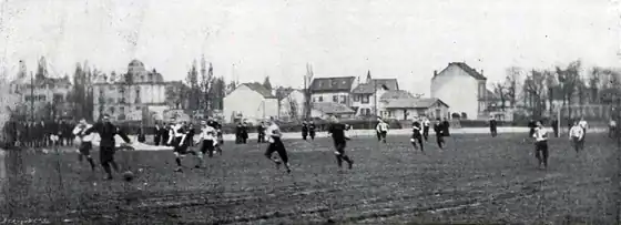 Photo en noir et blanc d'un match de football, sur la gauche, un joueur tout en noir a le ballon.