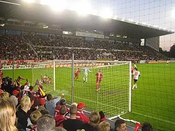 Photo d'un match de football prise depuis la tribune basse derrière le côté droit des buts.
