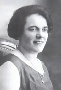Photo en noir et blanc de jeune femme brune d'environ 35 ans, souriante, avec médaille en pendentif.
