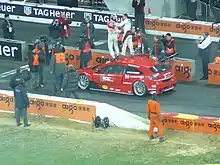 Photographie d'une voiture rouge sur laquelle deux pilotes se tiennent debout.