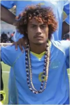 Photographie d'un homme, de face, en plan américain, avec un maillot bleu ciel, et un collier.