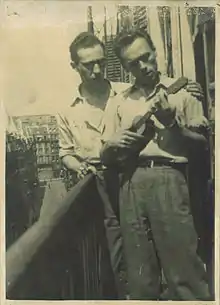 Photo sépia de 2 hommes jeunes debout sur un étroit balcon. Chemises et lunettes années 1940 ou 1950.