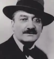 Photographie en gros plan et en noir et blanc d'un homme moustachu portant un chapeau et un monocle.