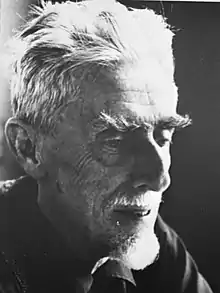 Photographie en noir et blanc d'un vieil homme aux cheveux blancs et avec des rides.