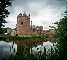 Photo d'un bâtiment imposant aux murs de brique rouge avec une grande tour d'angle, entouré d'eau