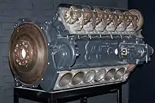 Photographie en couleur d’un moteur Maybach HL210 peint en gris et présenté isolément sur un socle.