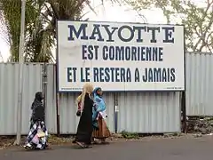 La devise sous l'écu, « Ra Hachiri » (« Nous sommes vigilants ») vient des revendications des Comores sur Mayotte (ici sur un panneau à Moroni).