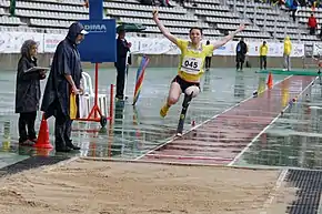 Athlète handisport atterrissant au saut en longueur, de face, les bras en l'air.