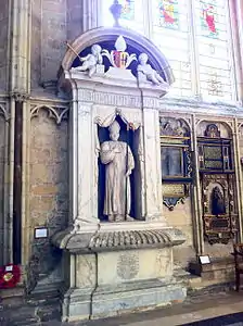 Photo d'une statue d'homme encadrée de colonnes surplombées de chérubins, le tout en pierre blanche et surplombant un tombeau