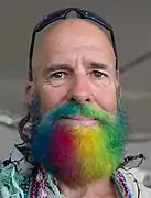 Un homme avec une barbe arc-en-ciel lors d'une parade. Juin 2018.