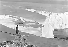 Homme à ski se tenant devant une falaise de glace.
