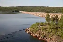 Un grand barrage retenant un lac, entouré de forêts.