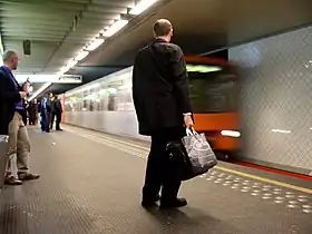 un quai avec des personnes qui attendent le métro, une rame arrive dans la station.
