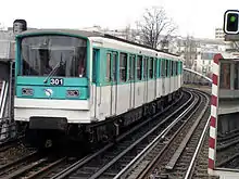 Photographie d'une rame de métro turquoise et blanche en circulation sur une partie aérienne de la ligne