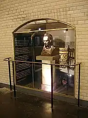 Photographie présentant une paroi faïencée au sein de laquelle se trouve un buste d'homme derrière une plaque de verre