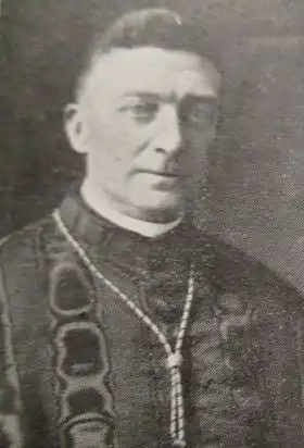 Photographie en noir et blanc d'un homme glabre de trois-quarts face en habit ecclésiastique, un cordon autour du cou.