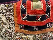 Vêtement féminin, de l'ethnie Miao. Application de tissus découpés selon le motif (blanc, rouge et rose), broderie de soie au point de croix. Yunnan Provincial Museum (en), Kunming.