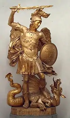 Photographie en couleurs d'une sculpture dorée représentant un personnage ailé et recouvert d'une armure, épée levée et bouclier serré contre l'abdomen, un dragon étendu à ses pieds.