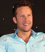 Homme brun souriant en chemise bleu clair.