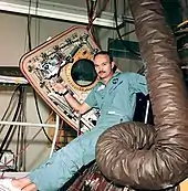 Photographie couleur de Collins assis sur l'écoutille de son module et tenant le panneau ouvert.