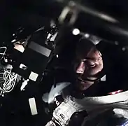 Photographie en couleur de Michael Collins dans le module de commande et de service avec le visage partiellement éclairé.