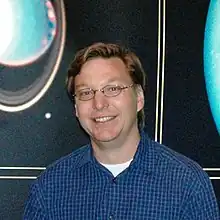 Photographie d'un homme souriant en chemise et avec des lunettes.