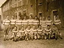 Photo sépia représentant 15 personnes devant un bâtiment en briques des années 1930 avec deux grandes portes.