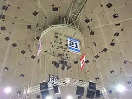 Photo de la bannière dédiée à Michel Briere au milieu de câbles tombant du plafond de la Mellon Arena; on distingue également les drapeaux américains, canadiens et la bannière dédiée à Mario Lemieux.