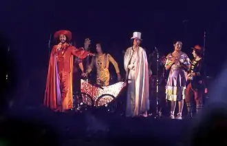 Six personnes sur scène portant des costumes de spectacle.