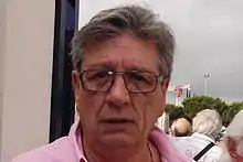 Photographie du visage d'un homme vu de face portant des lunettes et une chemise rose.
