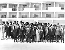 Groupe d'hommes et de femmes photographiés de face devant un bâtiment à étages