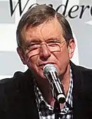 Un homme d'une soixantaine d'années aux cheveux courts avec des lunettes parlant devant un micro.