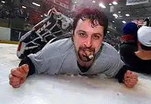 Photographie couleur d’un gardien de hockey allongé sur le ventre, face à l’objectif, avec un cigare à la bouche.