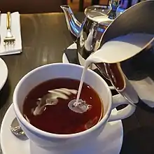 On verse du lait d’un pichet dans une tasse de thé sombre.