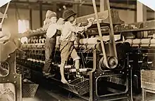  un jeune garçon pieds nus grimpé sur la machine vérifie une bobine de fil. Un autre, plus âgé, regarde l'objectif