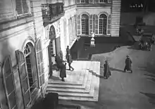 Photo en noir et blanc du perron d’un bâtiment, dans lequel pénètre un individu en civil et un militaire