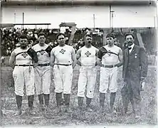 Photographie de cinq hommes posant en vêtement de sport à côté desquels se trouve un homme en costume