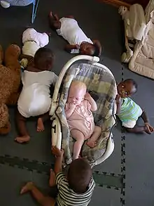 Bébé à peau blanche et cheveux jaune pâle au milieu d'autres bébés à peau brune et cheveux noirs