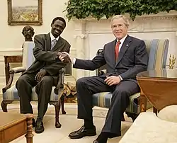 Deux homme en costume assis sur des fauteuils se serrent la main