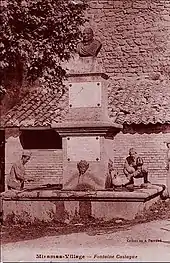 Photographie sépia d'une fontaine au cœur d'un bassin carré, surmontée d'un monument avec deux plaques de marbre et un buste.
