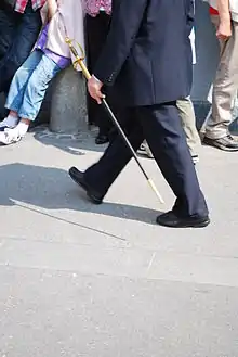 Photographie d'une personne marchant, portant un épée à bout de bras gauche.