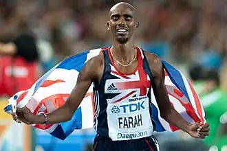 Mo Farah tenant un drapeau britannique qui flotte dans son dos.