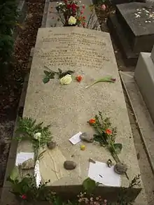 Photo d'une pierre tombale sobre avec des fleurs, des cailloux et des petits mots