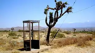 Cabine téléphonique dégradée dans un paysage de végétation sèche, avec au loin des montagnes.