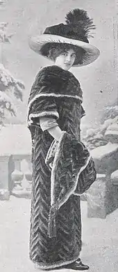 Photographie en noir et blanc d'un portrait en pied d'une femme portant avec élégance un manteau de fourrure en 1911.
