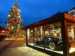 Voiture de luxe placée dans un container transparent sur une place éclairée de décorations de Noël.